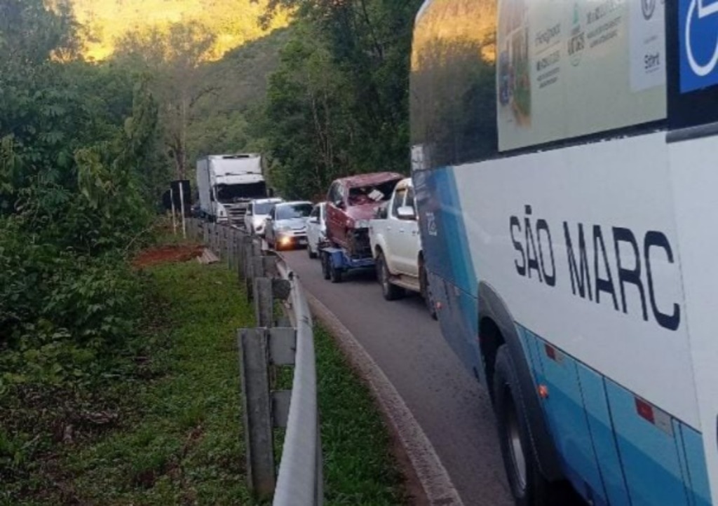 Fila de carros, trens e ônibus parados na BR-116, em área cercada por vegetação, durante obras de contenção em São Marcos