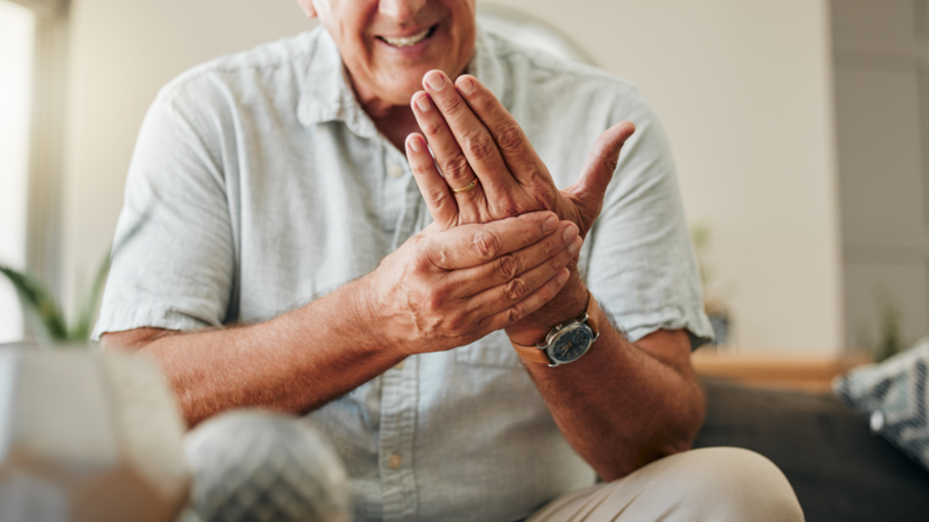 Pessoa madura com expressão de dor nas mãos, representando sintomas da fibromialgia.