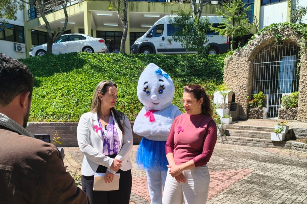 Secretária da Saúde de São Marcos e enfermeira responsável pela Vigilância Epidemiológica concedem entrevista ao São Marcos Online, com a personagem Maria Gotinha ao fundo, em frente à Secretaria Municipal da Saúde.